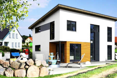 Modernes Einfamilienhaus mit Flachdach, weißen Fassaden und Holzverkleidung, davor Garten mit Liegestühlen und Steinmauer.