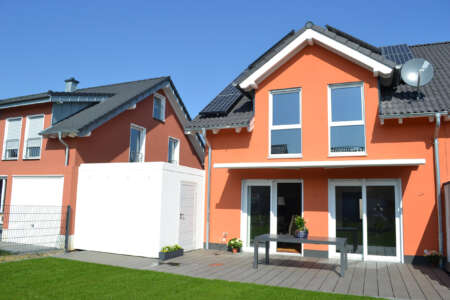 Einfamilienhaus mit oranger Fassade, Terrasse und Solarpanels.