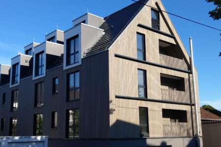 Mehrfamilienhaus mit moderner Holzfassade und markanten Dachgauben in Fellbach bei Sonnenschein.