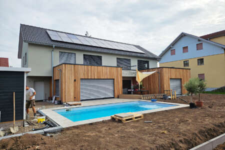 Modernes Einfamilienhaus mit Holzverkleidung, Solaranlage und Pool in Bauphase.