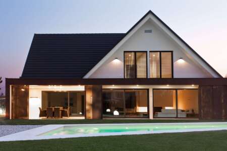 Modernes Einfamilienhaus mit großer Glasfront und Pool im Garten, beleuchtet in der Abenddämmerung.
