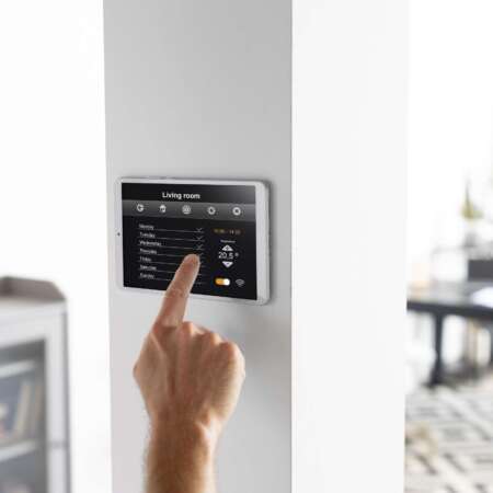 Hand bedient Wand-Tablet zur Steuerung eines Smart-Home-Systems im Wohnzimmer.
