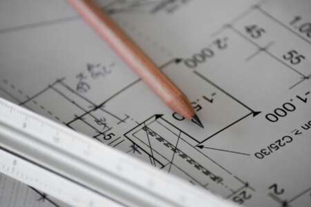 Nahaufnahme eines technischen Bauplans mit Maßangaben, ein Bleistift und ein Architektenlineal liegen auf dem Papier.
