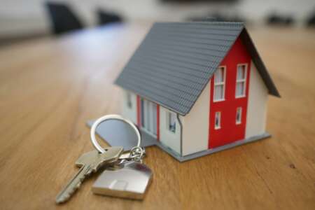 Modellhaus mit Schlüsselbund auf Holztisch – Symbol für Hauskauf oder Immobilienfinanzierung.